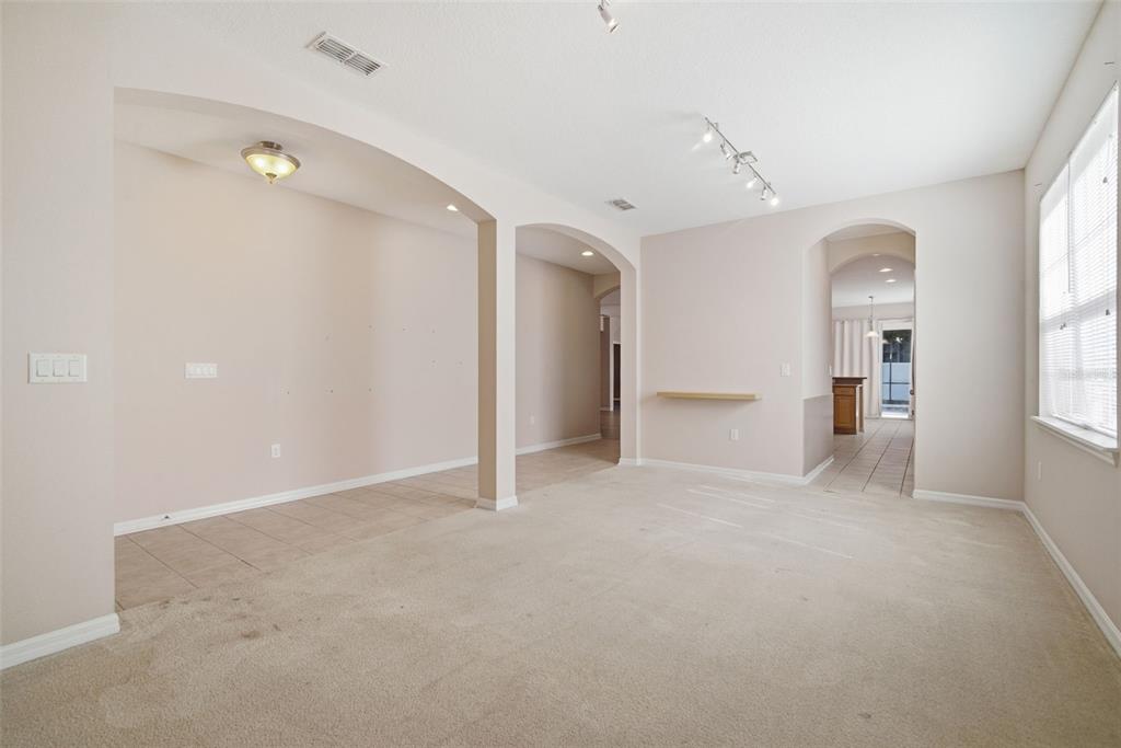 An empty living room features beige carpet, tiled flooring, arched doorways, and a wall-mounted shelf — 1520 RHODESWELL LANE, DOVER, FL