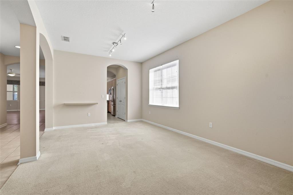 An empty living room with beige carpet, light-colored walls, a window, and a wall-mounted shelf — 1520 RHODESWELL LANE, DOVER, FL