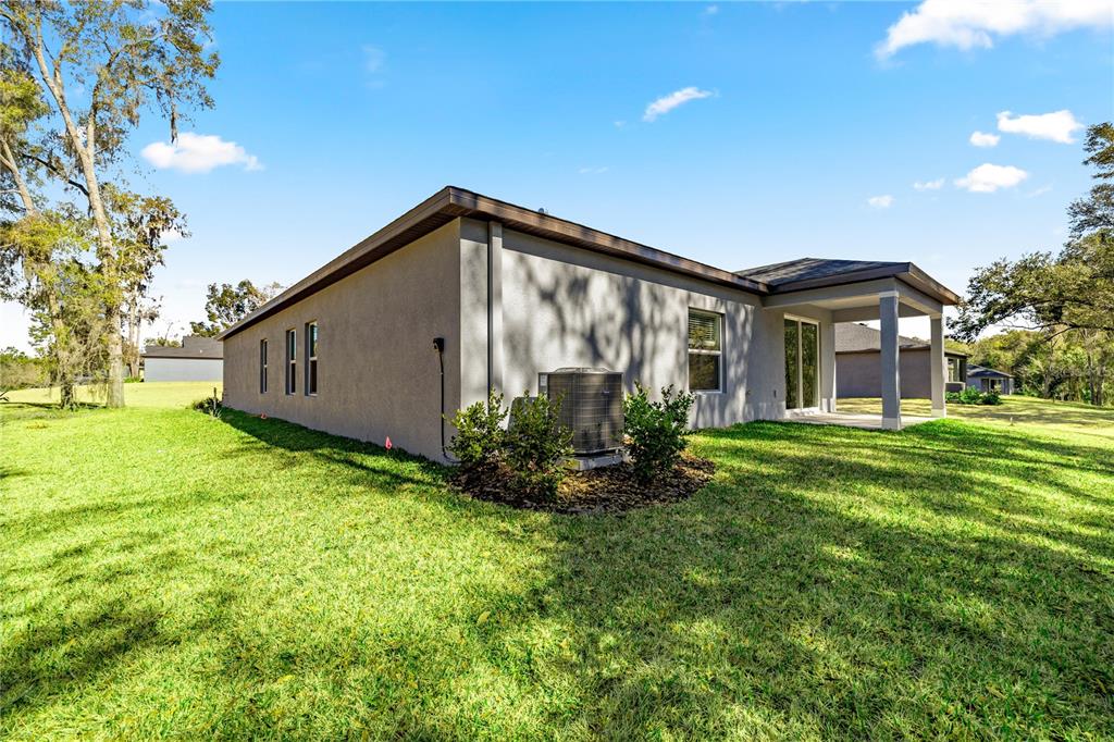 The exterior of a gray stucco house features a covered patio and an HVAC unit — 8363 SW 197TH COURT, DUNNELLON, FL