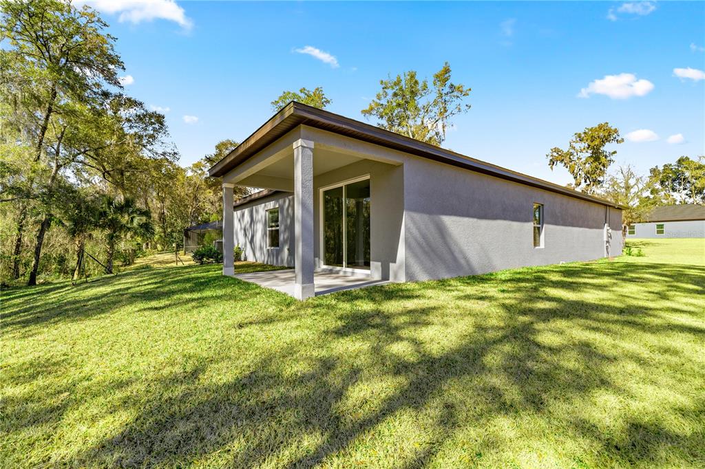The exterior of a house features a covered concrete patio and a grassy backyard — 8363 SW 197TH COURT, DUNNELLON, FL