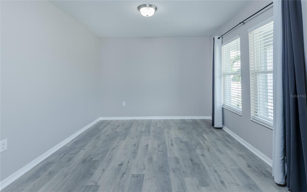 An empty room with light gray walls, gray wood-look flooring, and two windows with curtains — 1916 SW 12TH TERRACE, CAPE CORAL, FL