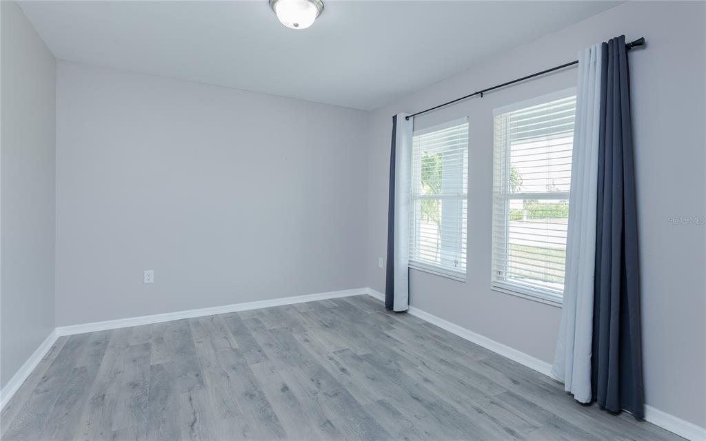 An empty room features gray walls, wood-look flooring, and two windows with dark curtains — 1916 SW 12TH TERRACE, CAPE CORAL, FL
