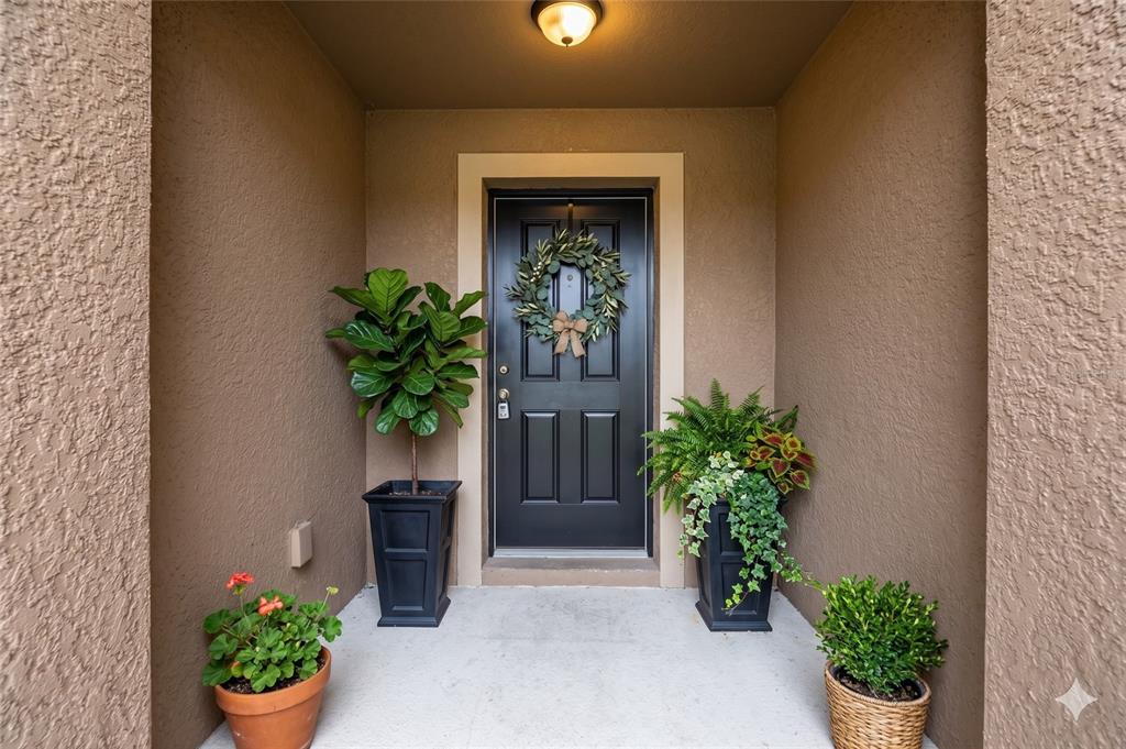 A black front door with a wreath is flanked by potted plants on a porch — 9139 SW 60TH COURT ROAD, OCALA, FL