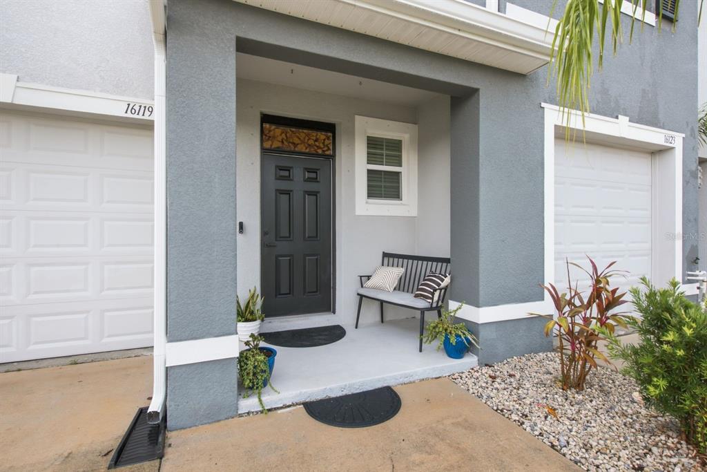 A gray front door with a transom window sits between two white garage doors — 16119 GLOWING GROVE AVENUE, ODESSA, FL