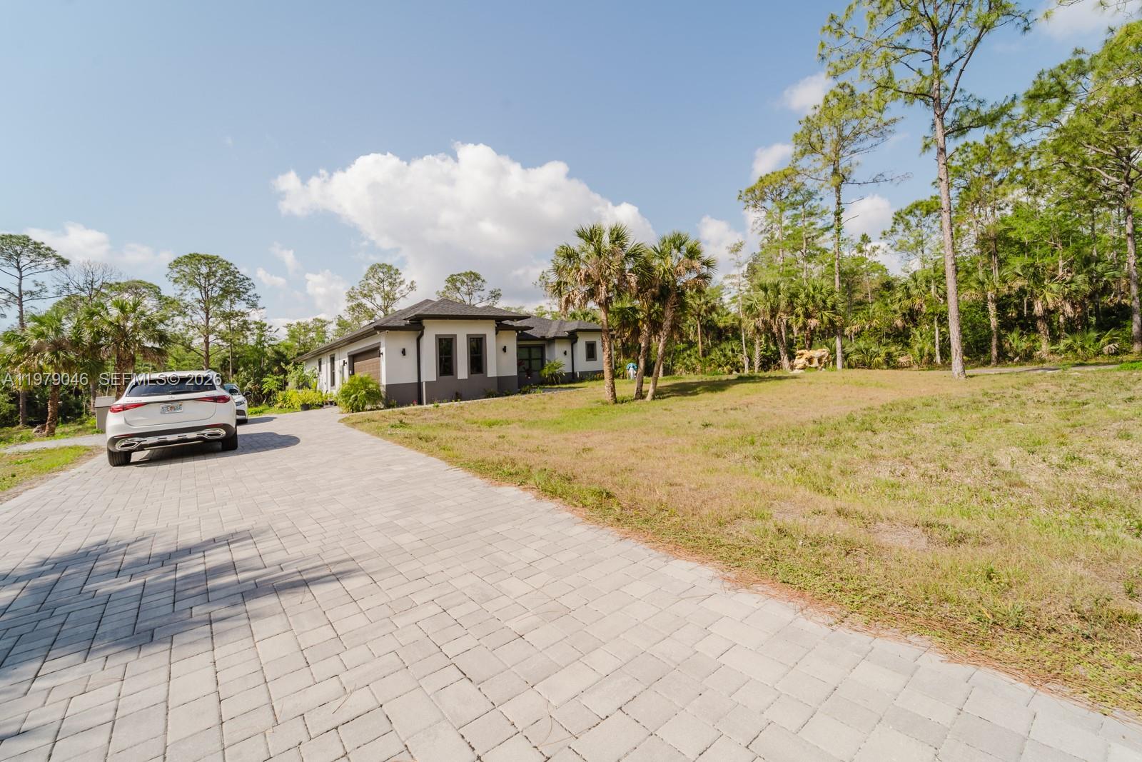 A white house with a paved driveway sits on a large, grassy lot with trees — 398 35th Ave NW, Naples FL 34120, NAPLES, FL
