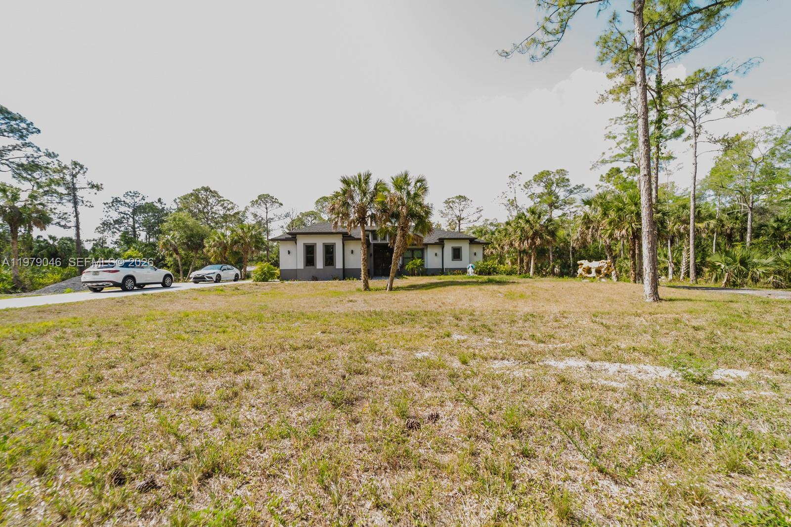 A modern single-story house sits on a large, grassy lot surrounded by pine trees — 398 35th Ave NW, Naples FL 34120, NAPLES, FL
