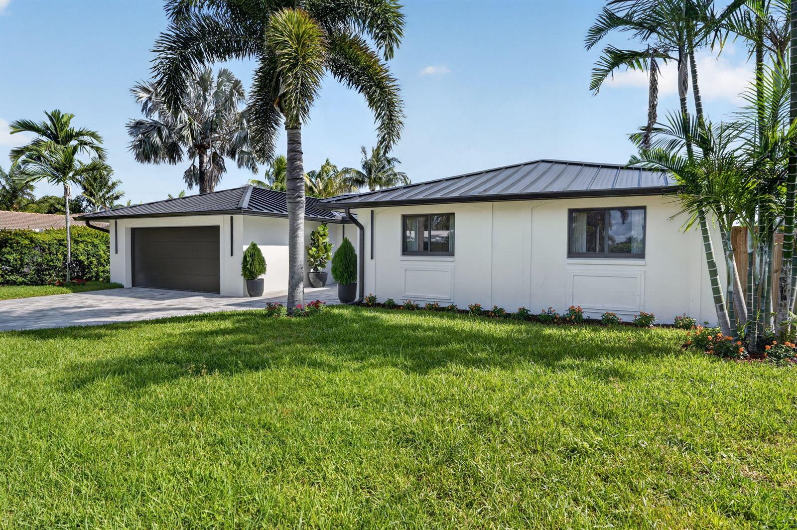 A single-story white house with a dark metal roof, garage, and palm trees — 1803 Juno Isles Boulevard, North Palm Beach FL 33408, NORTH PALM BEACH, FL