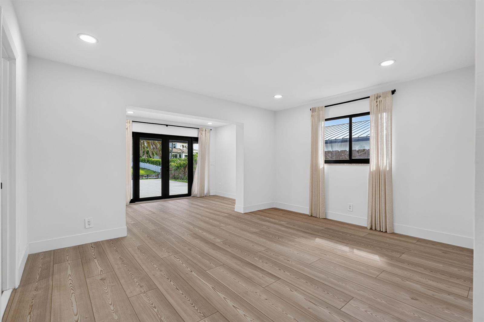 An empty room with light wood-look flooring, white walls, recessed lighting, and glass patio doors — 1803 Juno Isles Boulevard, North Palm Beach FL 33408, NORTH PALM BEACH, FL