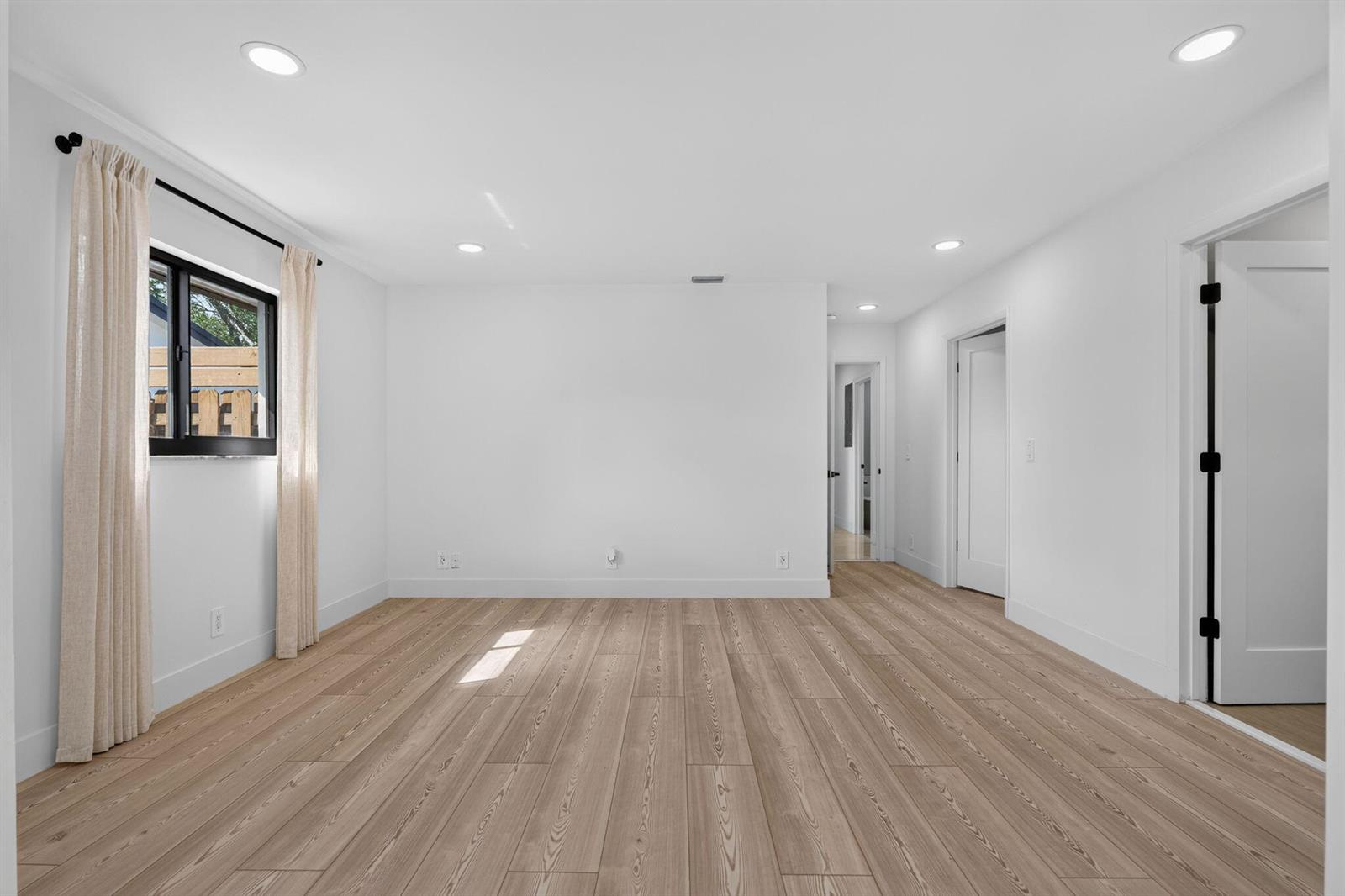 An empty room with white walls, light wood-look flooring, recessed lighting, and a window — 1803 Juno Isles Boulevard, North Palm Beach FL 33408, NORTH PALM BEACH, FL