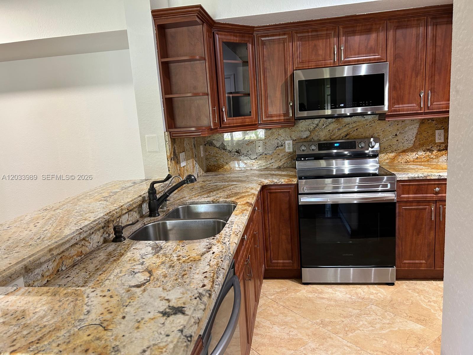 A kitchen features dark wood cabinets, granite countertops, and stainless steel appliances — 2516 Centergate Dr # 102, Miramar FL 33025, MIRAMAR, FL