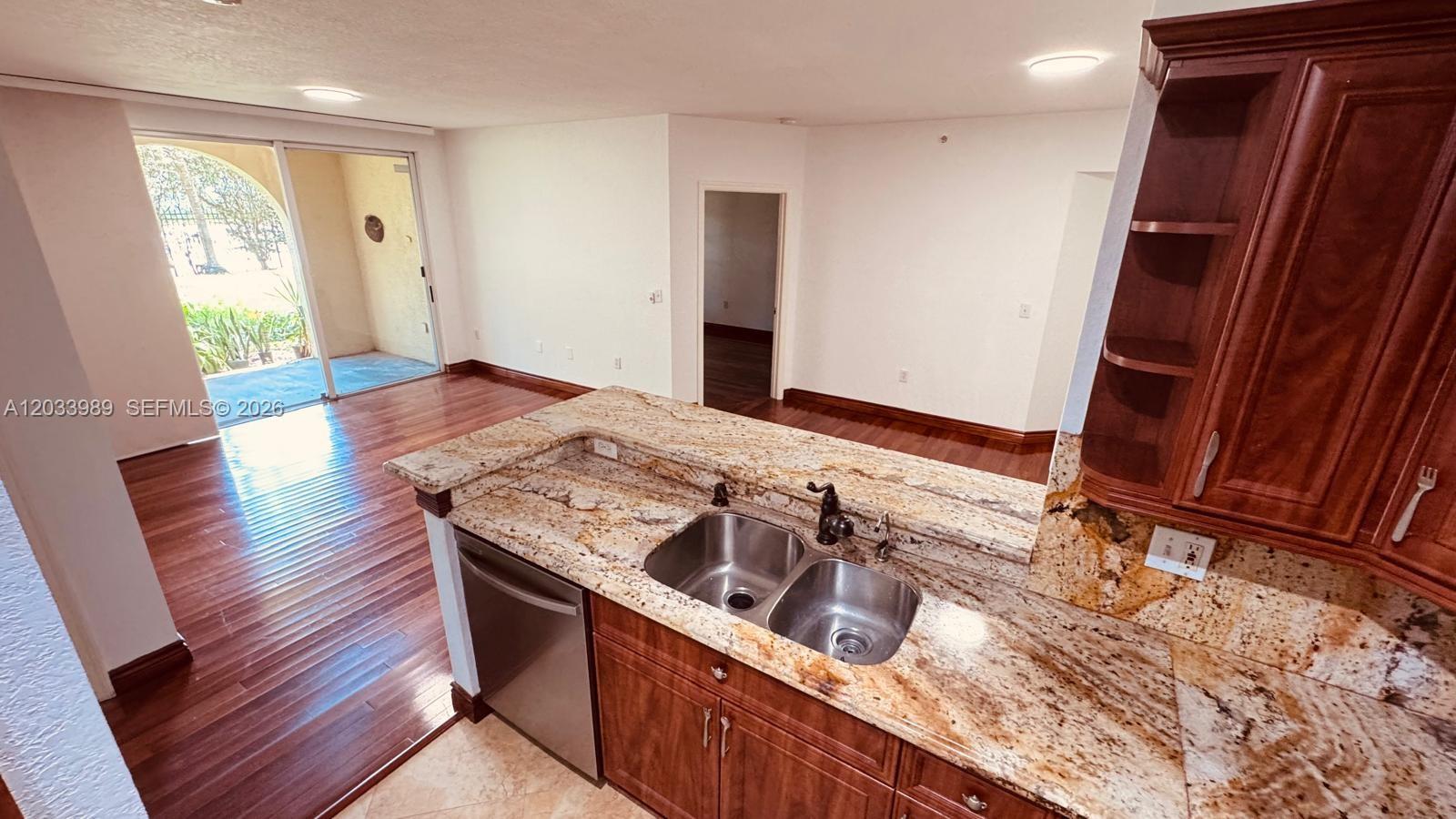 A kitchen with granite countertops and wooden cabinets overlooks a living area with hardwood floors — 2516 Centergate Dr # 102, Miramar FL 33025, MIRAMAR, FL