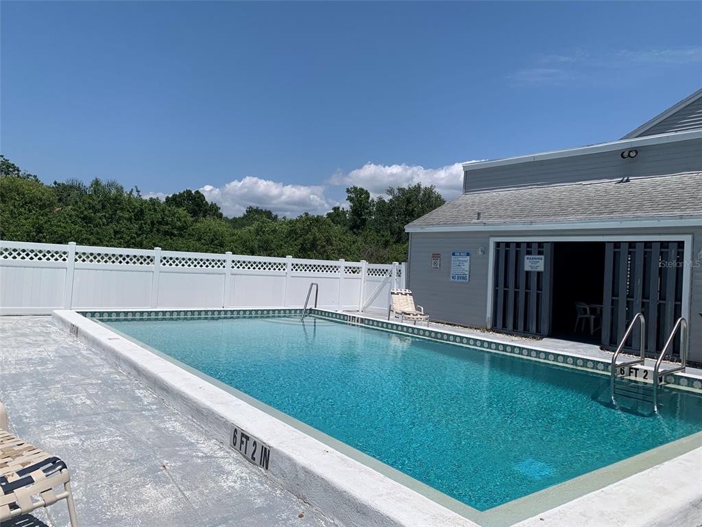An outdoor rectangular swimming pool with a white fence and a nearby building — 255 FENWICK DRIVE UNIT 18, VENICE, FL