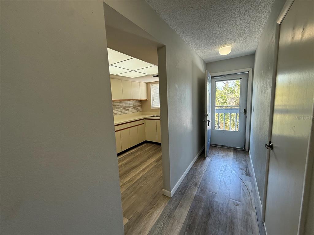 A hallway with wood-look flooring leads to a kitchen and an exterior door — 255 FENWICK DRIVE UNIT 18, VENICE, FL