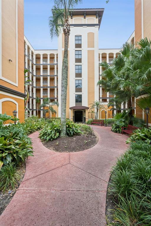 A paved walkway leads toward the entrance of a multi-story apartment building with tropical landscaping — 12538 FLORIDAYS RESORT DRIVE UNIT 109C, ORLANDO, FL