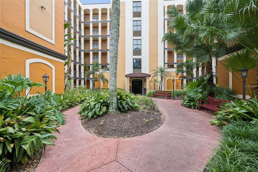 A paved walkway leads through a landscaped courtyard toward the entrance of a multi-story building — 12538 FLORIDAYS RESORT DRIVE UNIT 109C, ORLANDO, FL