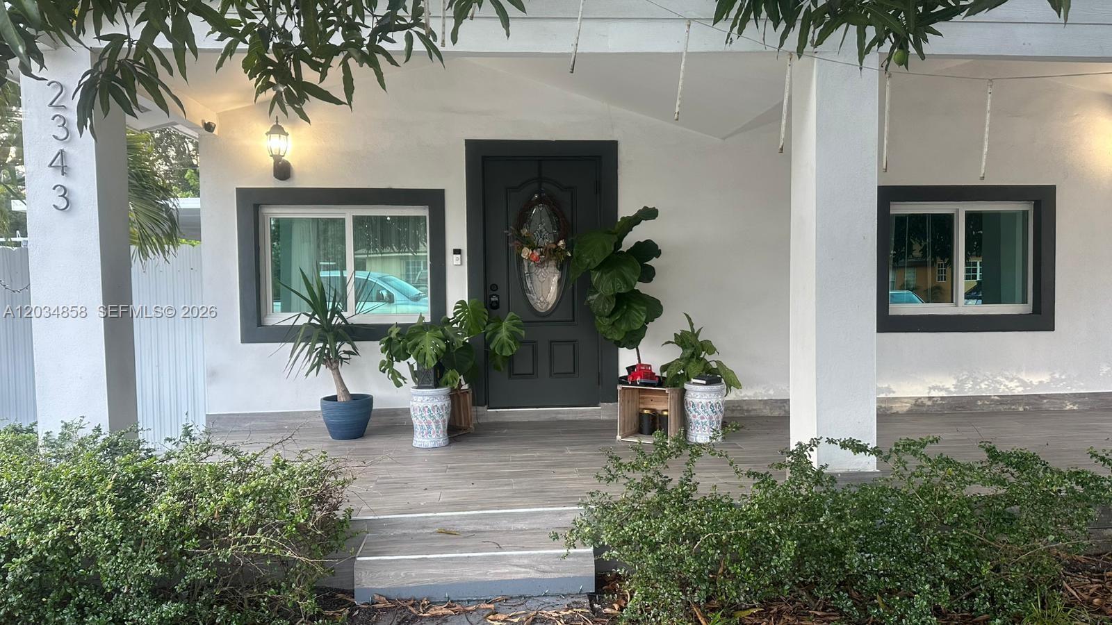 The exterior of a house features a covered porch, a dark front door, and potted plants — 2343 NW 102nd St, Miami FL 33147, MIAMI, FL
