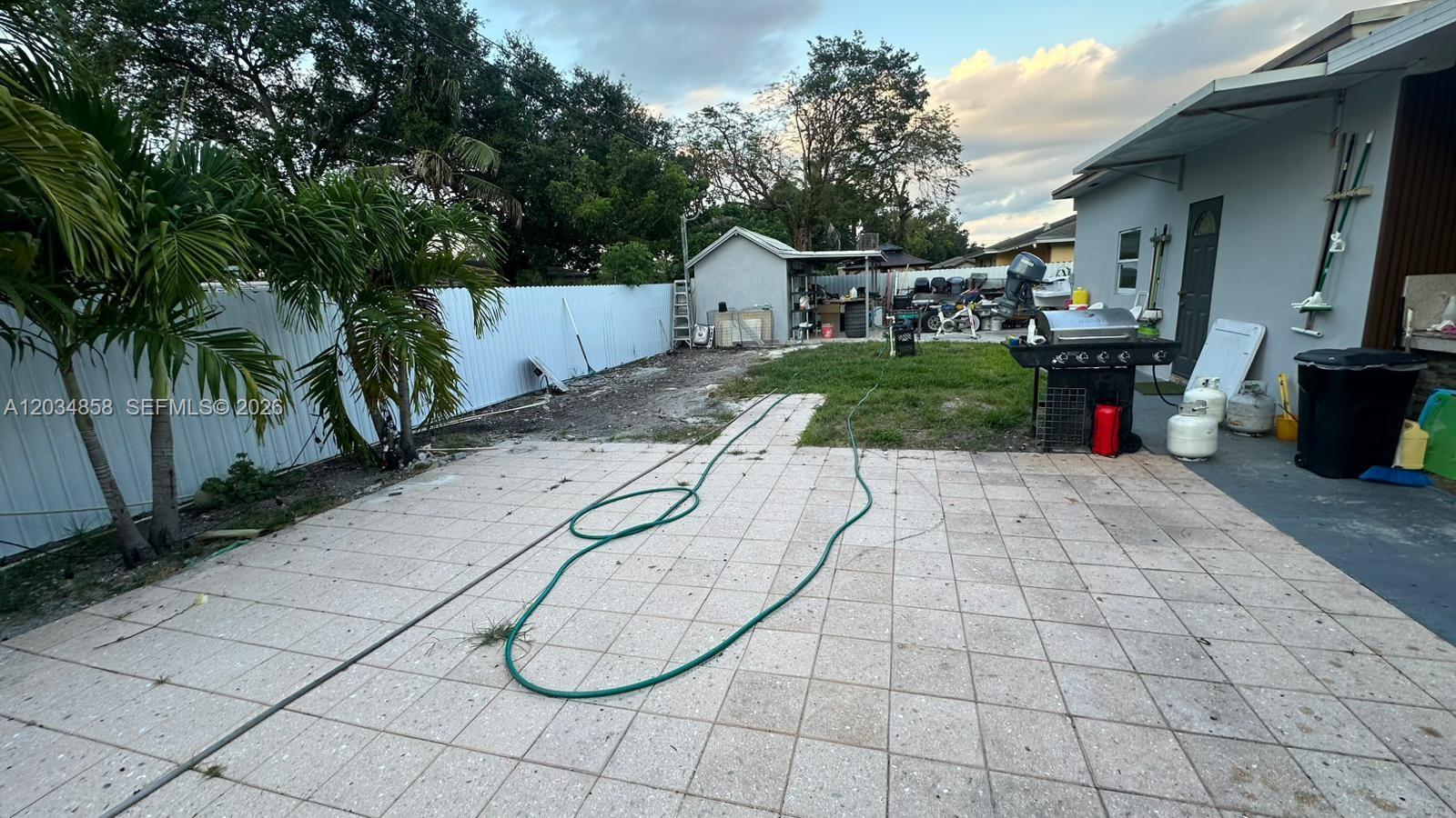 A paved patio leads to a grassy backyard with a shed and a white fence — 2343 NW 102nd St, Miami FL 33147, MIAMI, FL