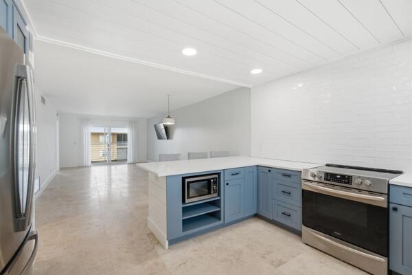 A kitchen with blue cabinets, white countertops, and a stainless steel stove opens to a living area — 308 Golfview Road, North Palm Beach FL 33408, NORTH PALM BEACH, FL