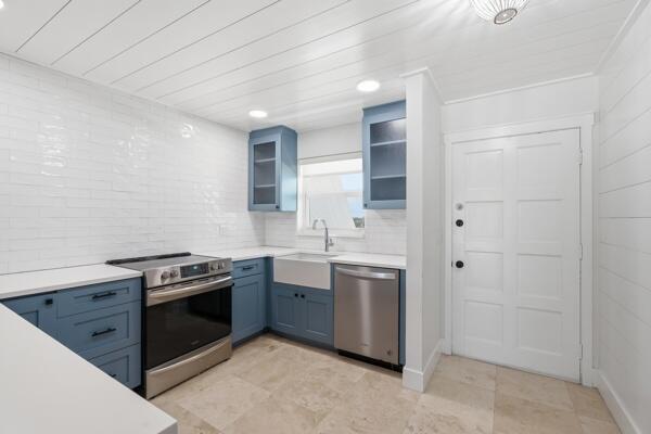 A kitchen features blue cabinets, white subway tile walls, a farmhouse sink, and stainless appliances — 308 Golfview Road, North Palm Beach FL 33408, NORTH PALM BEACH, FL