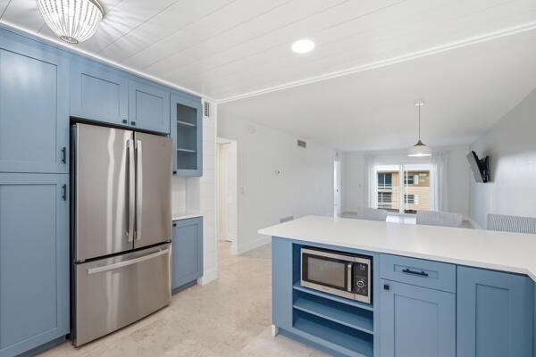 A kitchen features blue cabinets, stainless steel appliances, and a white island with a microwave — 308 Golfview Road, North Palm Beach FL 33408, NORTH PALM BEACH, FL