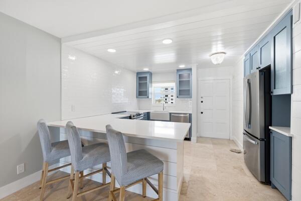 A kitchen features a white peninsula, blue cabinets, stainless steel appliances, and light tile flooring — 308 Golfview Road, North Palm Beach FL 33408, NORTH PALM BEACH, FL