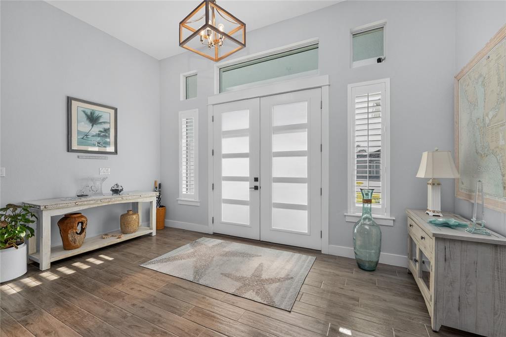 A bright entryway features double glass-paneled doors, wood-look tile flooring, and a coastal-themed rug — 9305 SPRING CIRCLE, PORT CHARLOTTE, FL