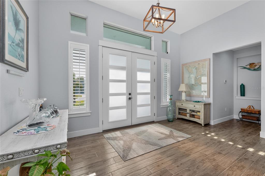 A bright entryway features a double front door, wood-look tile flooring, and a geometric chandelier — 9305 SPRING CIRCLE, PORT CHARLOTTE, FL