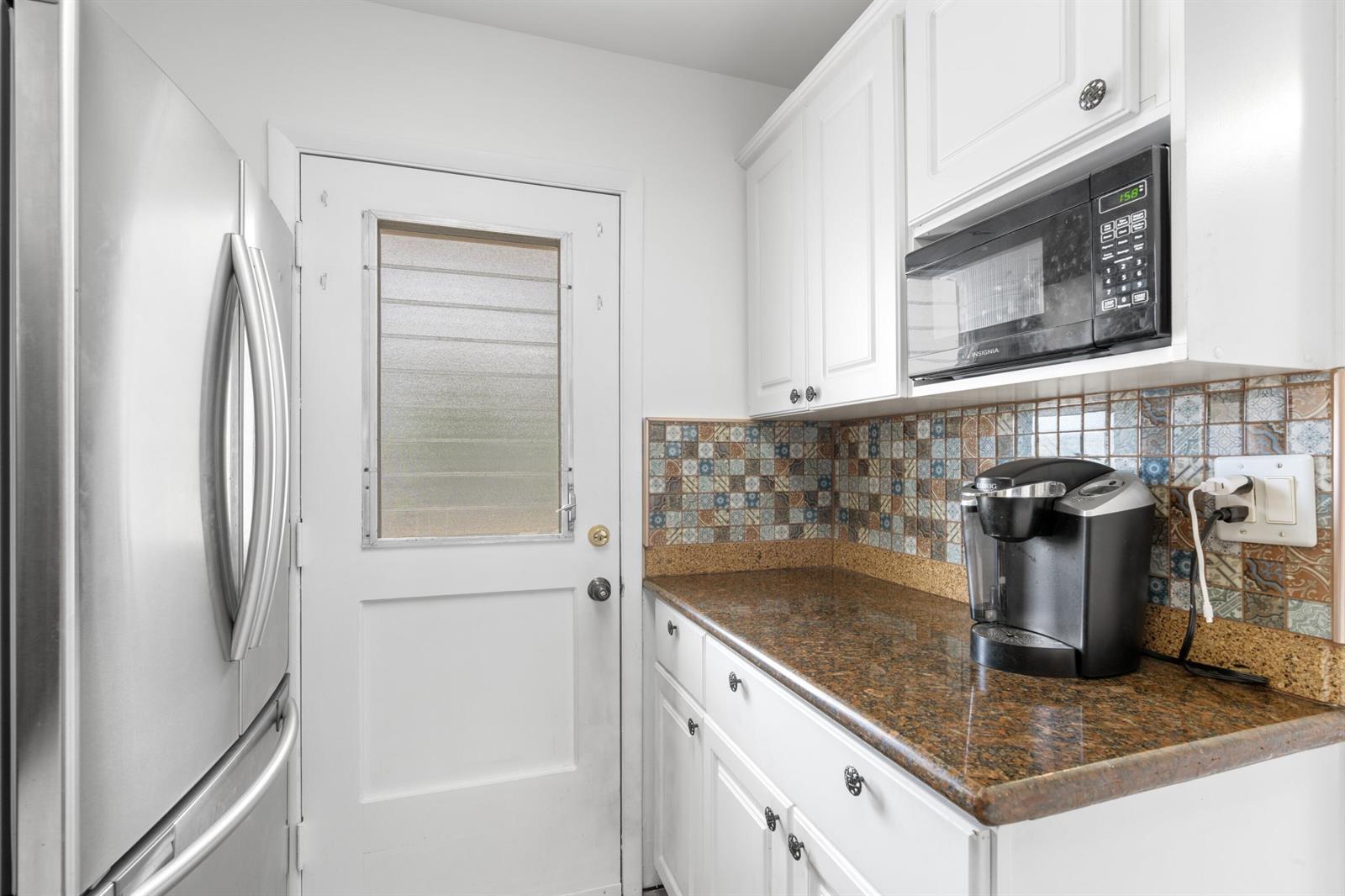 A kitchen features white cabinets, granite countertops, a patterned tile backsplash, and a glass-paneled door — 5501 NW 2nd Avenue # 2130, Boca Raton FL 33487, BOCA RATON, FL