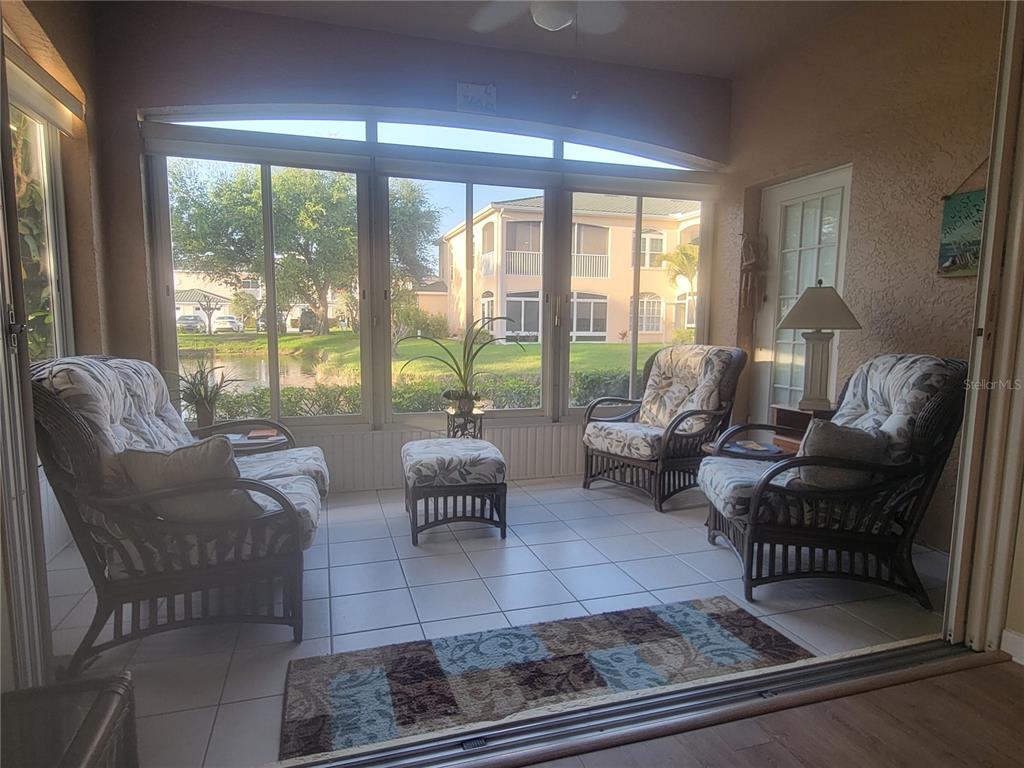 A sunroom with tile floors, wicker furniture, and large windows overlooking a pond and buildings — 1203 GONDOLA PARK DRIVE UNIT 1203, VENICE, FL