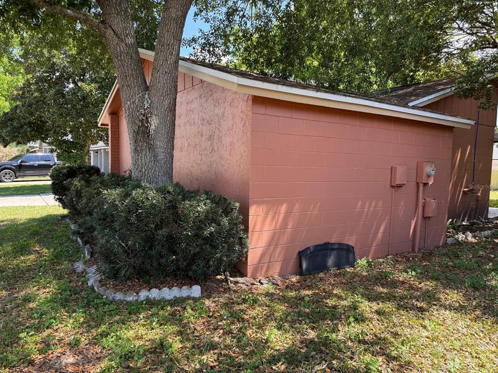 A side view of a house exterior with a concrete block wall and a large tree — 451 CART COURT, POINCIANA, FL
