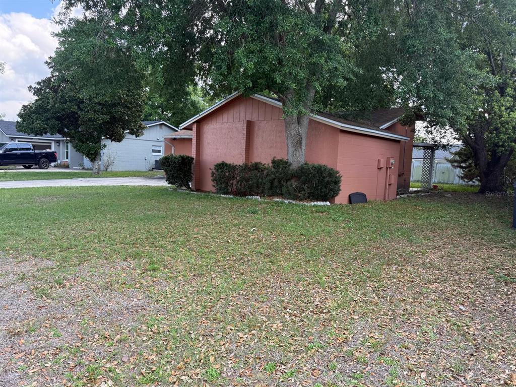 A side view of a peach-colored house with a large tree growing near the wall — 451 CART COURT, POINCIANA, FL