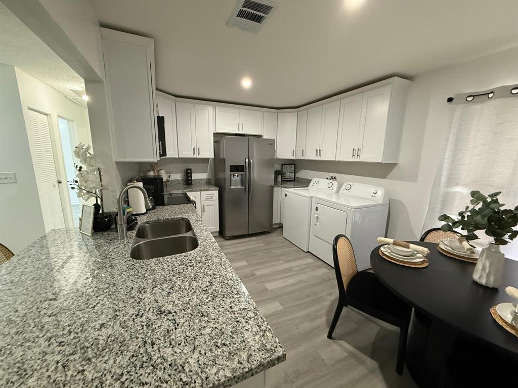 A kitchen with white cabinets, granite countertops, stainless steel appliances, and an adjacent laundry area — 451 CART COURT, POINCIANA, FL