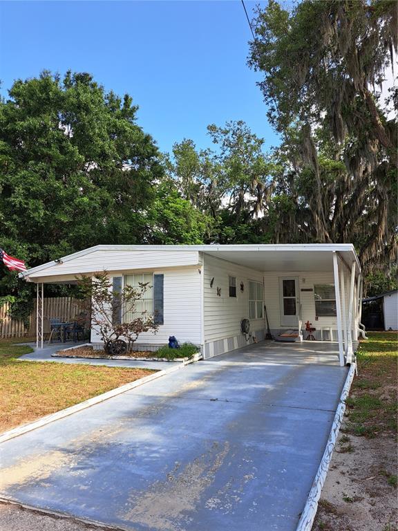 A single-story mobile home with a carport and a paved driveway under large trees — 119 DAISY AVENUE, AUBURNDALE, FL