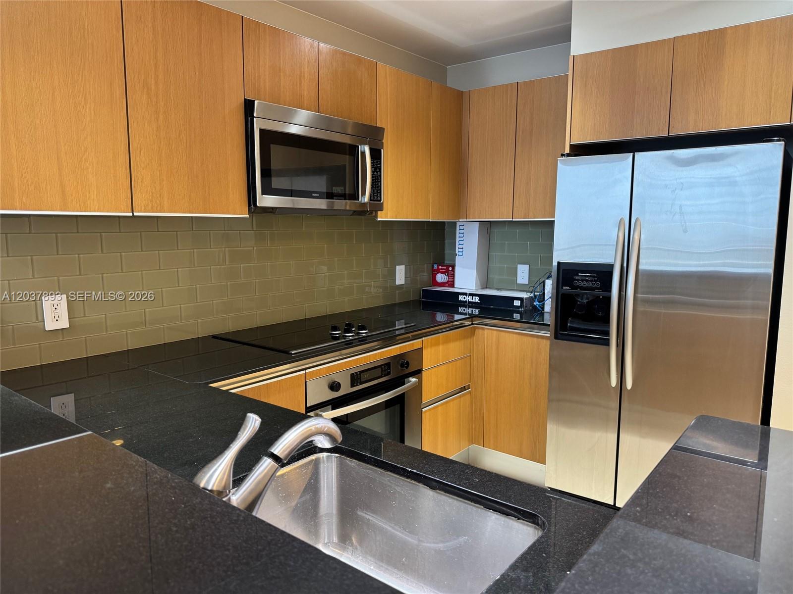 A kitchen features light wood cabinets, black countertops, stainless steel appliances, and olive green tile — 1060 Brickell Ave # 4115, Miami FL 33131, MIAMI, FL