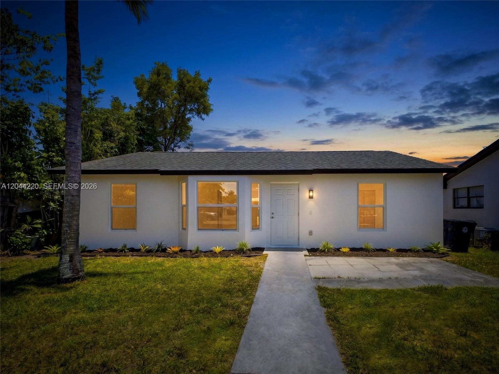 A single-story white house with a gray roof and a concrete walkway at dusk — 1229 18th Ave N, Lake Worth FL 33460, LAKE WORTH, FL