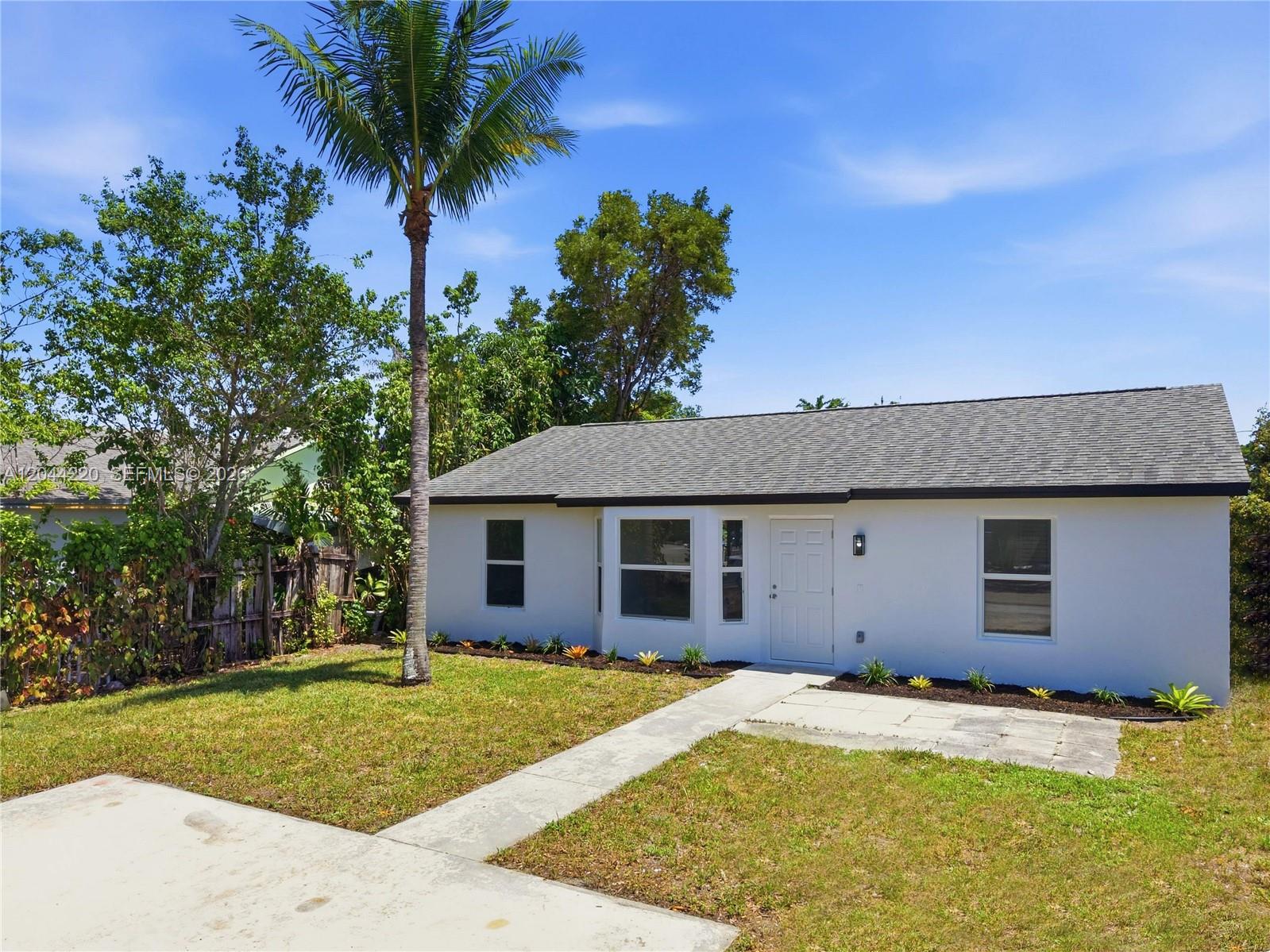 A white single-story house features a gray shingled roof, a palm tree, and a walkway — 1229 18th Ave N, Lake Worth FL 33460, LAKE WORTH, FL