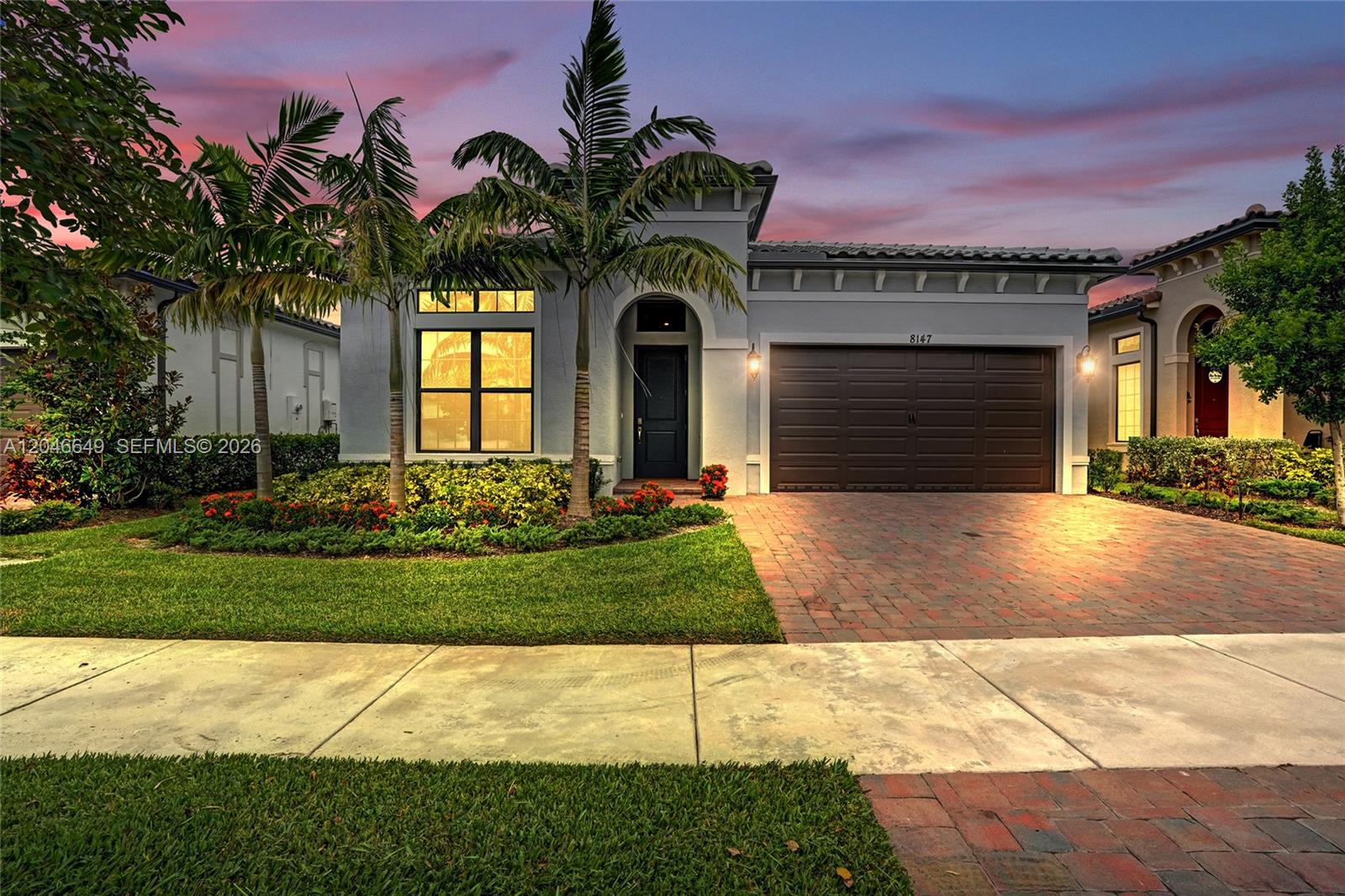 A single-story house with a brick driveway, a two-car garage, and palm trees at dusk — 8147 Juniper Dr, Parkland FL 33067, PARKLAND, FL