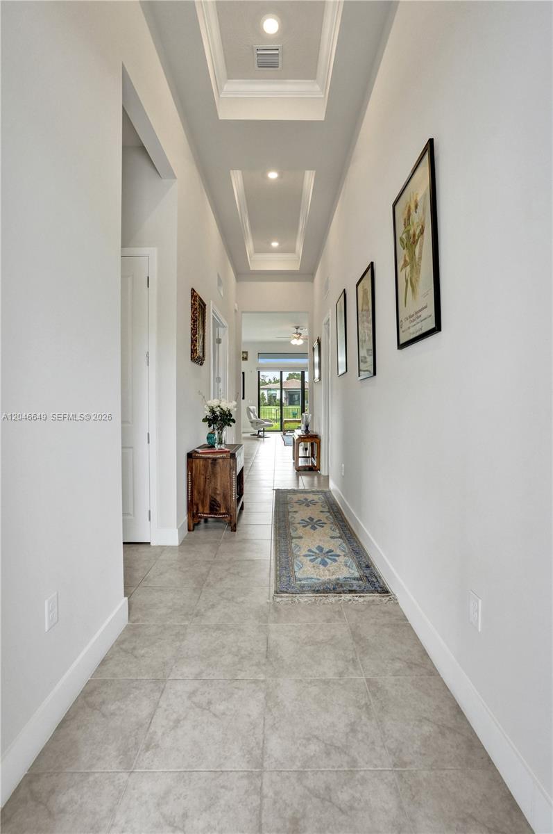 A long, tiled hallway features a tray ceiling, recessed lighting, and framed wall art — 8147 Juniper Dr, Parkland FL 33067, PARKLAND, FL