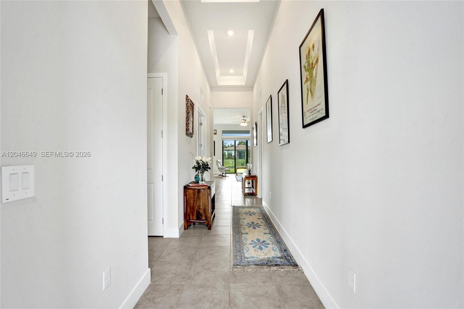 A bright, tiled hallway features a tray ceiling, framed wall art, and a runner rug — 8147 Juniper Dr, Parkland FL 33067, PARKLAND, FL