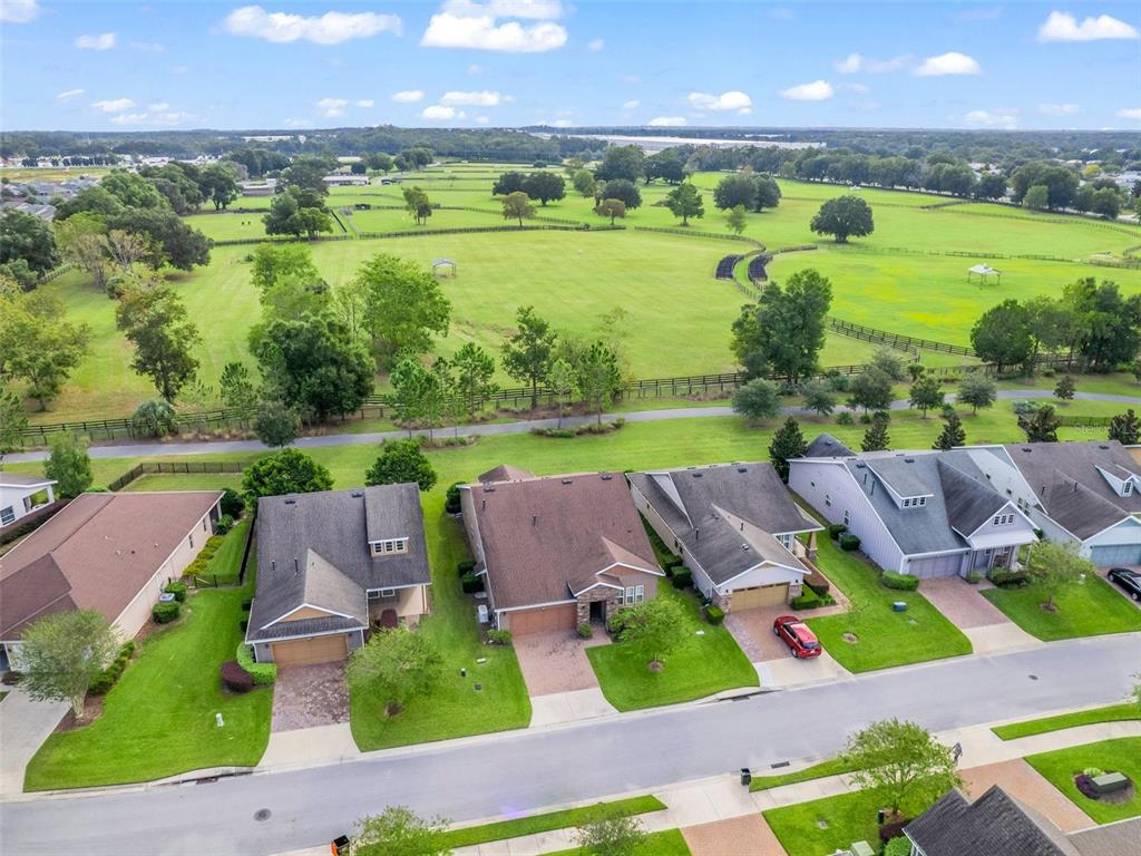 An aerial view shows a row of suburban houses bordering a large, open green pasture — 4976 NW 35TH LANE ROAD, OCALA, FL