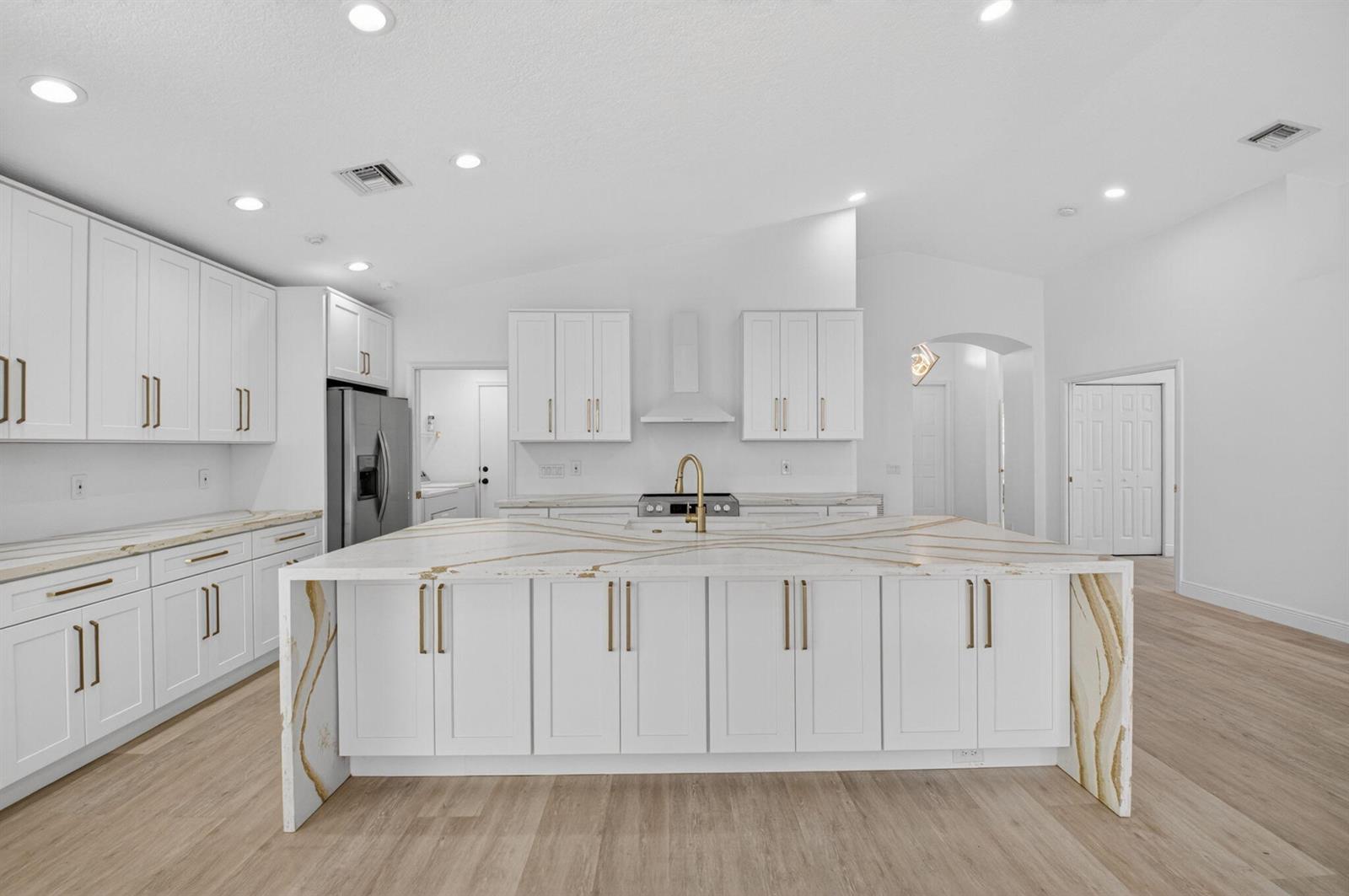 A bright kitchen features white cabinets, a large waterfall island with gold veining, and wood-look flooring — 11728 Dove Hollow Avenue, Boynton Beach FL 33437, BOYNTON BEACH, FL