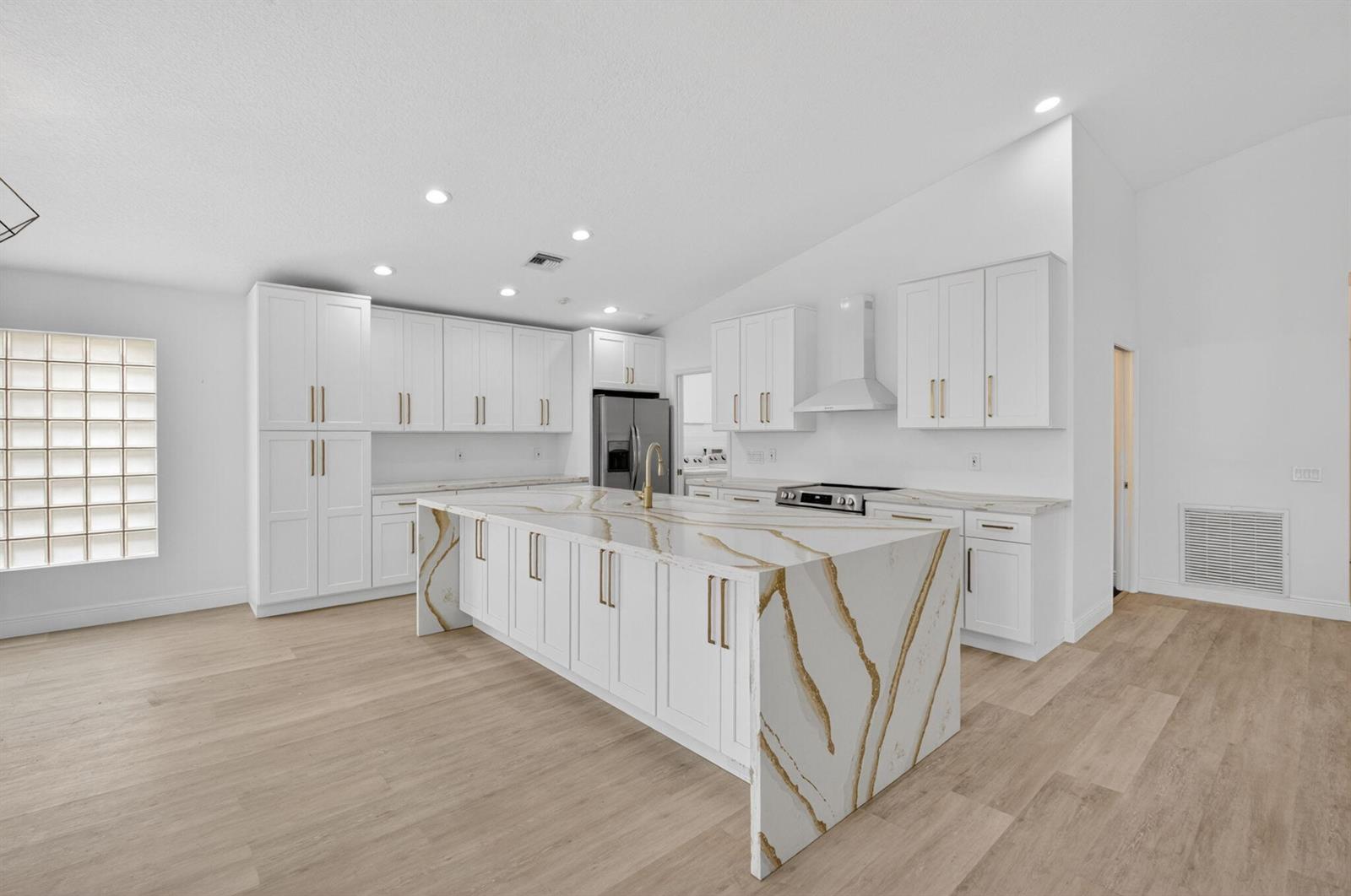 A modern kitchen features white cabinetry, gold hardware, and a large waterfall-edge marble island — 11728 Dove Hollow Avenue, Boynton Beach FL 33437, BOYNTON BEACH, FL