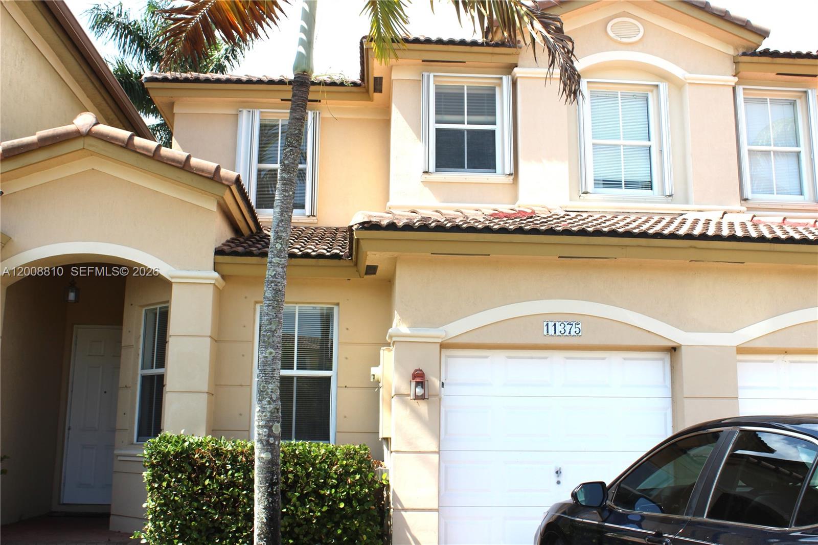 A two-story beige stucco townhouse features a white garage door and a palm tree — 11375 NW 77th Ln # 11375, Doral FL 33178, DORAL, FL