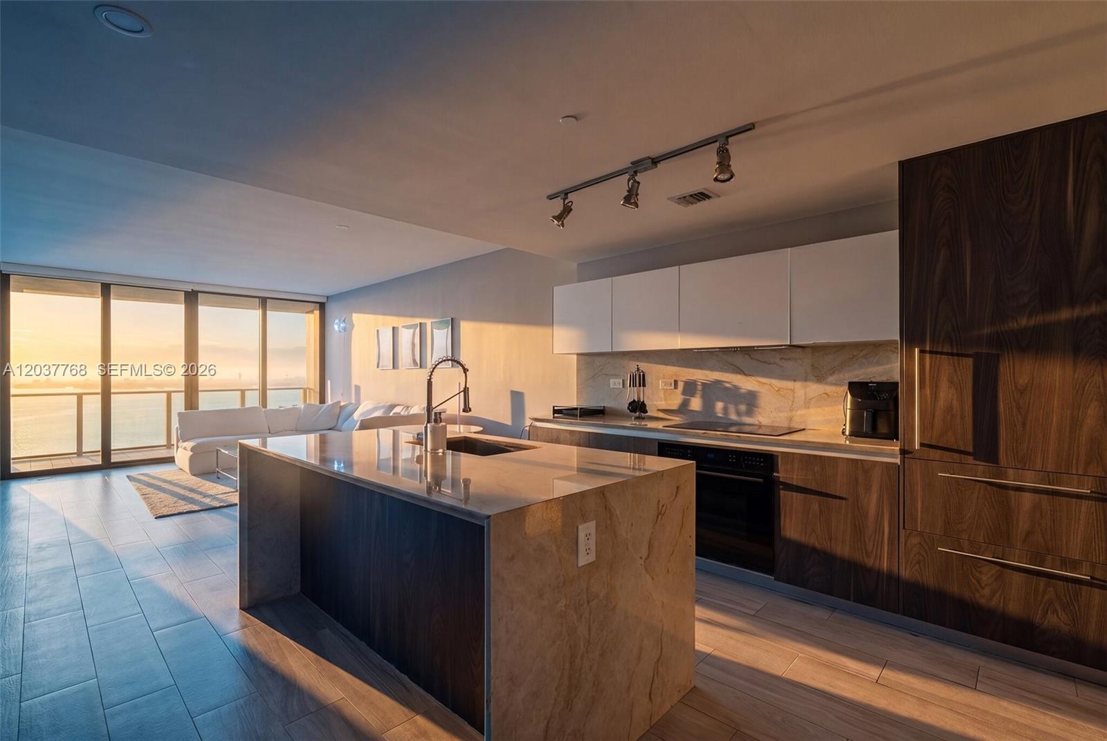 A modern kitchen with a stone island overlooks a living area with a water view — 3131 NE 7th Ave # 2402, Miami FL 33137, MIAMI, FL