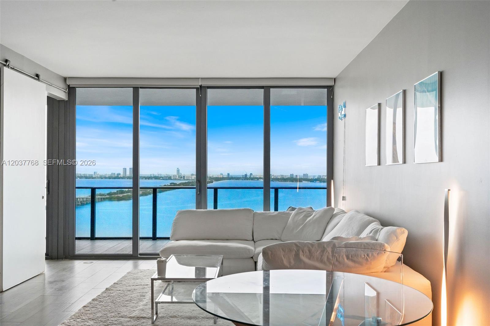 A living room with a white sectional sofa, glass tables, and floor-to-ceiling windows overlooking water — 3131 NE 7th Ave # 2402, Miami FL 33137, MIAMI, FL