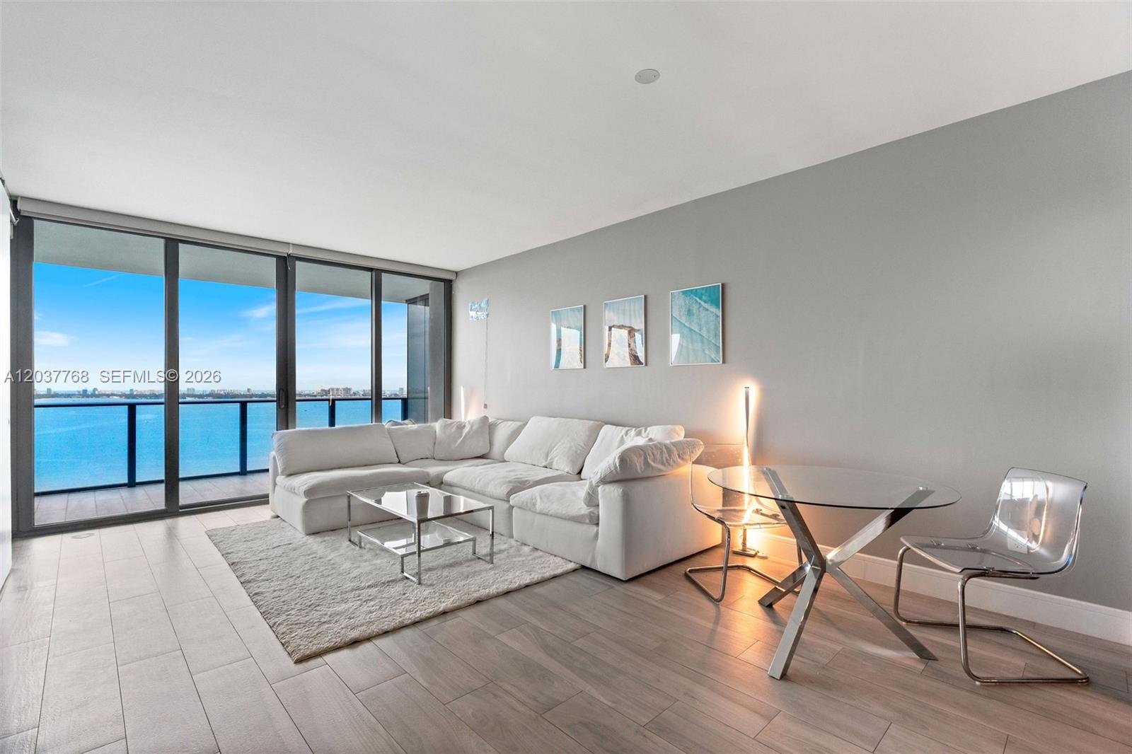 A balcony with a dining table and lounge chair overlooks a sunset over the water — 3131 NE 7th Ave # 2402, Miami FL 33137, MIAMI, FL