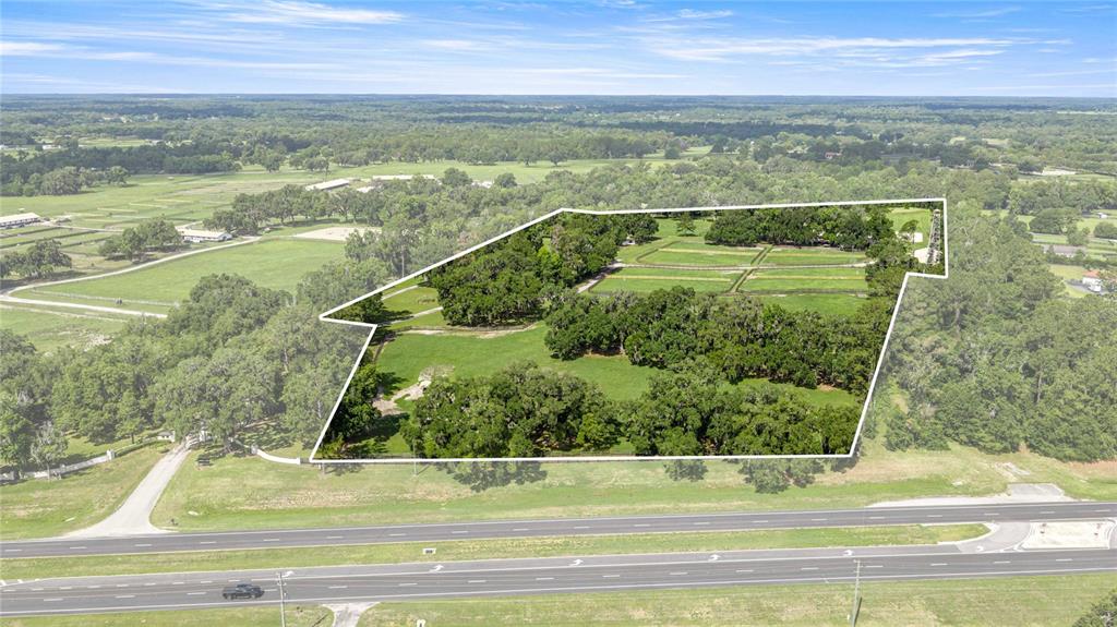 An aerial view shows a large, fenced grassy lot with many trees beside a highway — 12670 N US HIGHWAY 27, OCALA, FL
