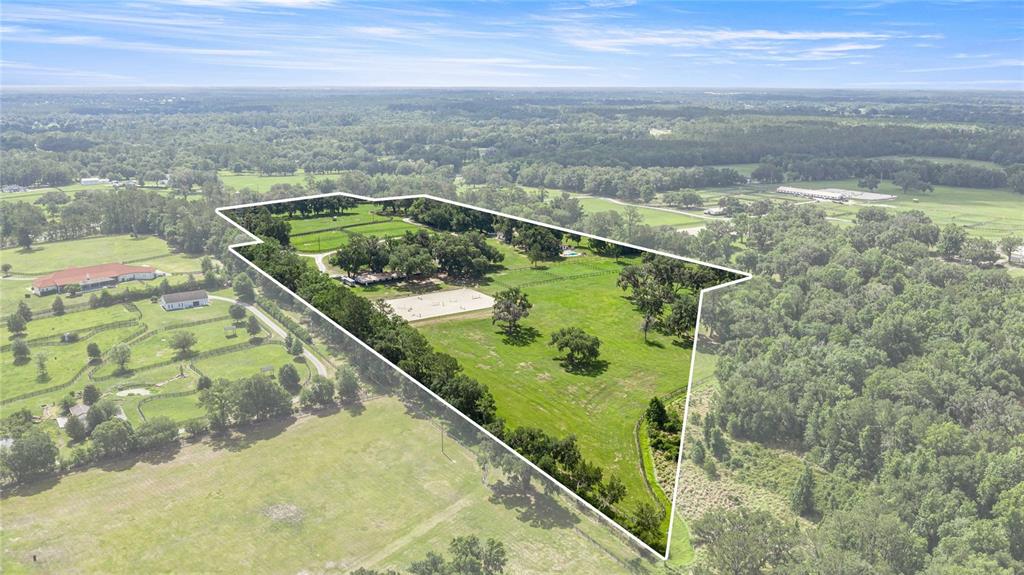 An aerial view shows a large, fenced rural property featuring a riding arena and trees — 12670 N US HIGHWAY 27, OCALA, FL