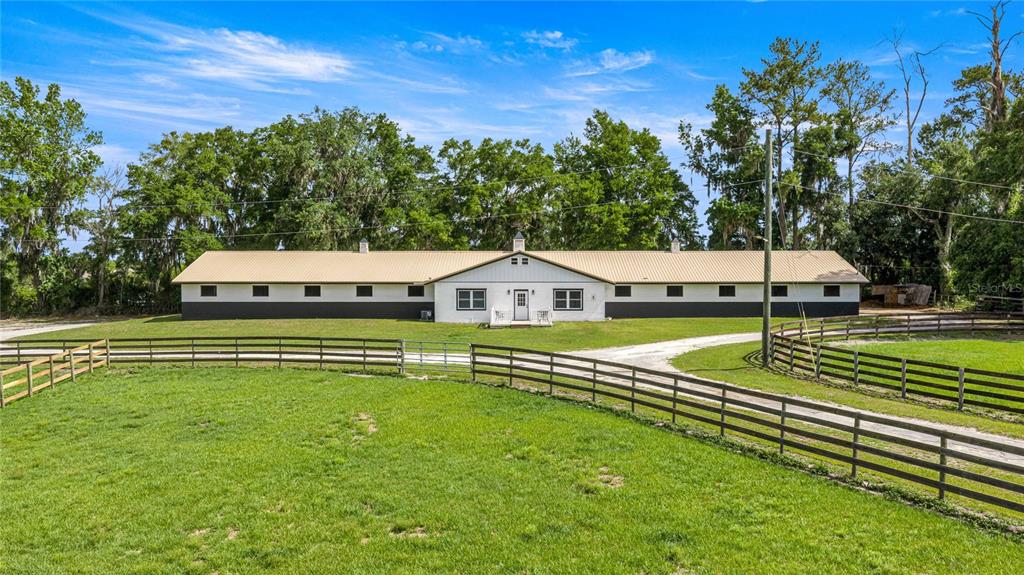 A long, single-story barn with a metal roof and fenced pasture in a rural setting — 12670 N US HIGHWAY 27, OCALA, FL