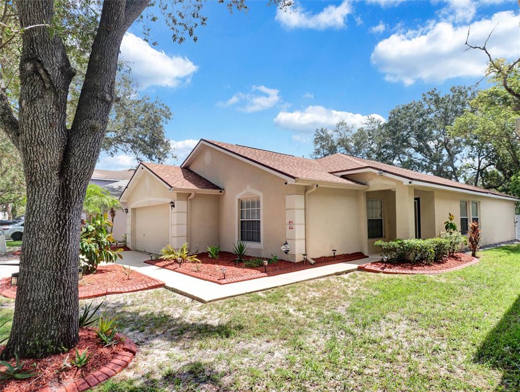 A single-story tan house with a two-car garage and red mulch landscaping — 7515 TERRACE RIVER DRIVE, TEMPLE TERRACE, FL
